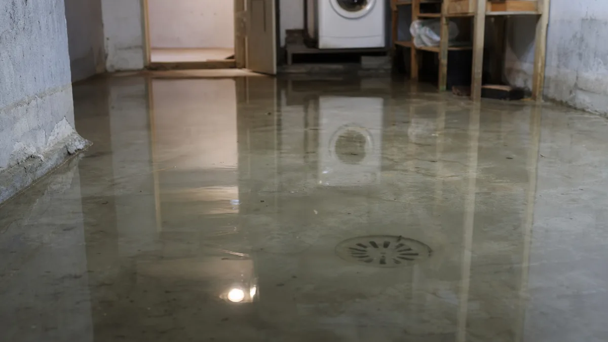 Mit Wasser überfluteter Keller, stehendes Abwasser auf Betonboden, sichtbarer Bodenablauf, gedämpfte Lichtverhältnisse
