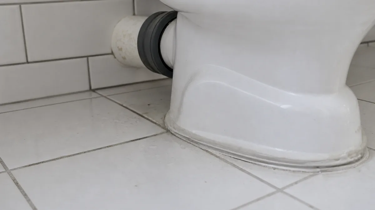 Detailaufnahme eines modernen WC-Beckens im Bad, von unten sichtbare Anschlussmanschette und Abflussrohr, helles sachliches Licht
